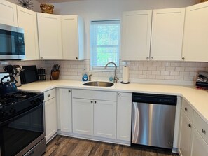 A modern kitchen with white cabinets, a stainless steel dishwasher, a gas stove, and a window with blinds. - Chic, coastal, pet-friendly retreat located in Lower Township, NJ. (Lower Township)
