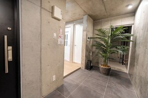 A hallway with a potted plant, a door, and a wall-mounted intercom.