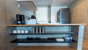 Cozinha compacta com cafeteira, canecas de aço inoxidável e geladeira.