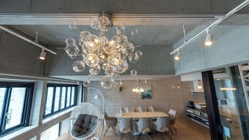 Um interior moderno com um lustre esférico único, uma área de refeições com mesa e cadeiras redondas, e uma cadeira de vime com almofada.