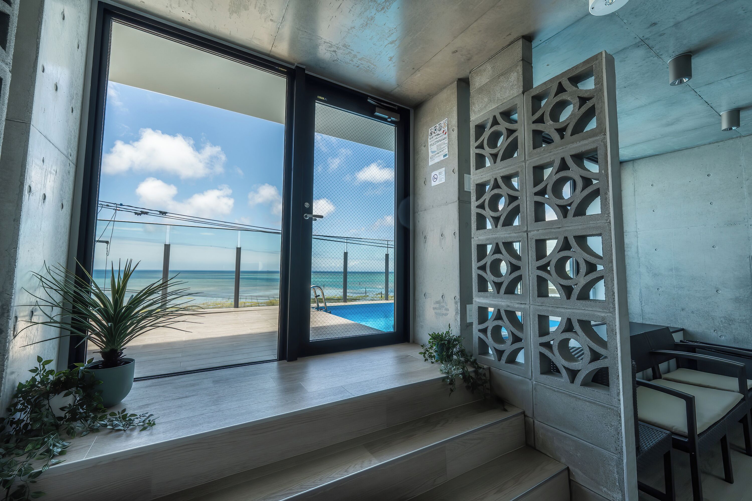 Un interior moderno con vista al océano, una piscina y una escalera que lleva a un espacio exterior.