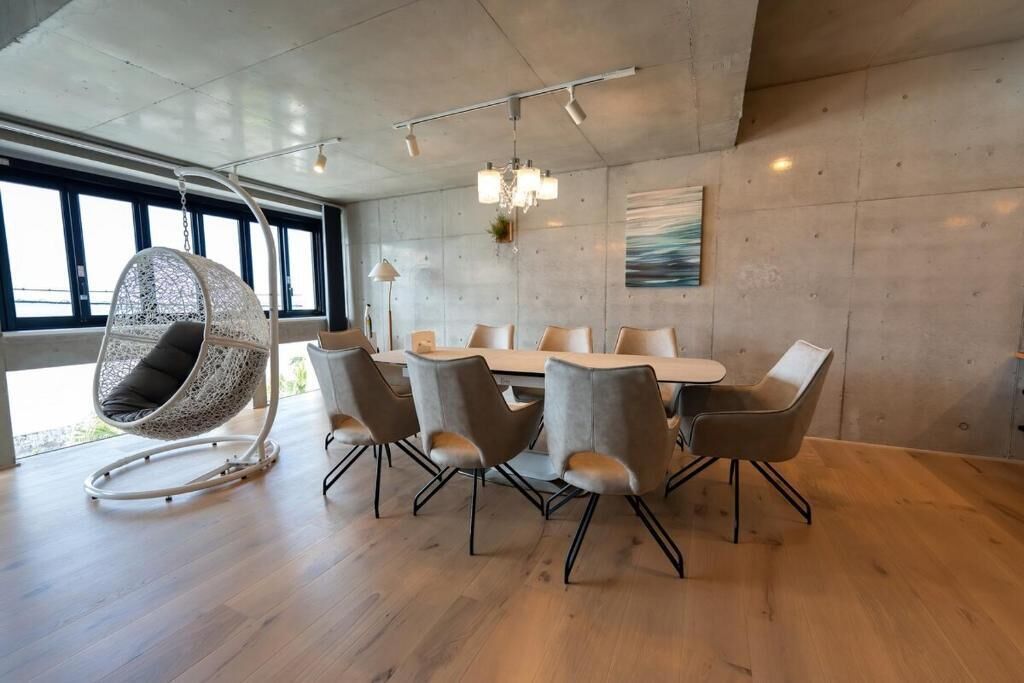 A modern dining area with a large table, six chairs, and a hanging chair.