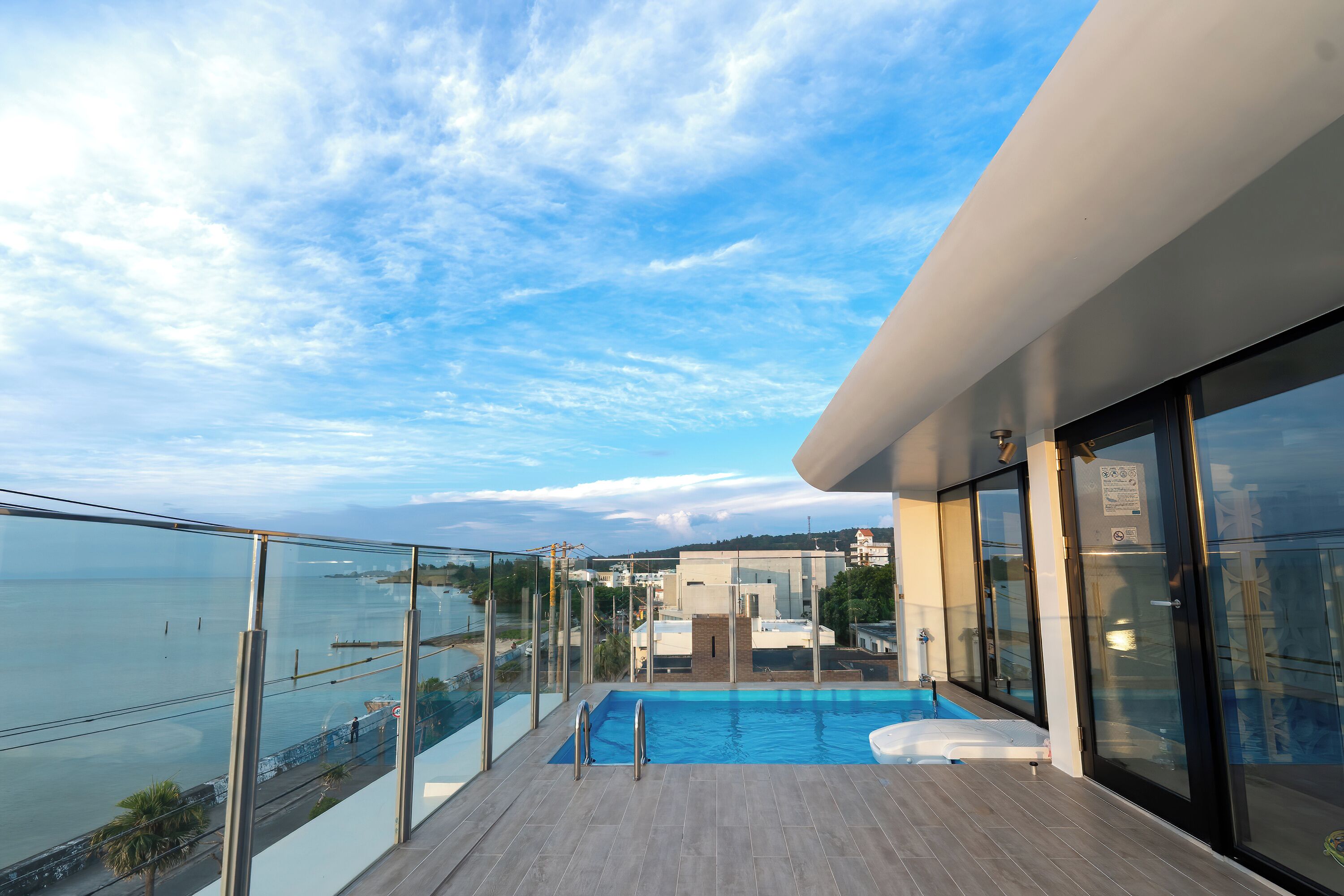 Varanda moderna com guarda-corpo de vidro, vista para uma piscina e um corpo de água.
