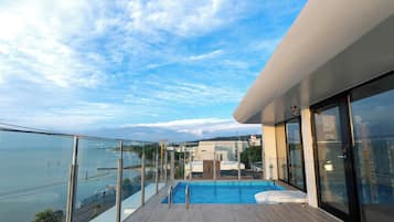Varanda moderna com guarda-corpo de vidro, vista para uma piscina e um corpo de água.