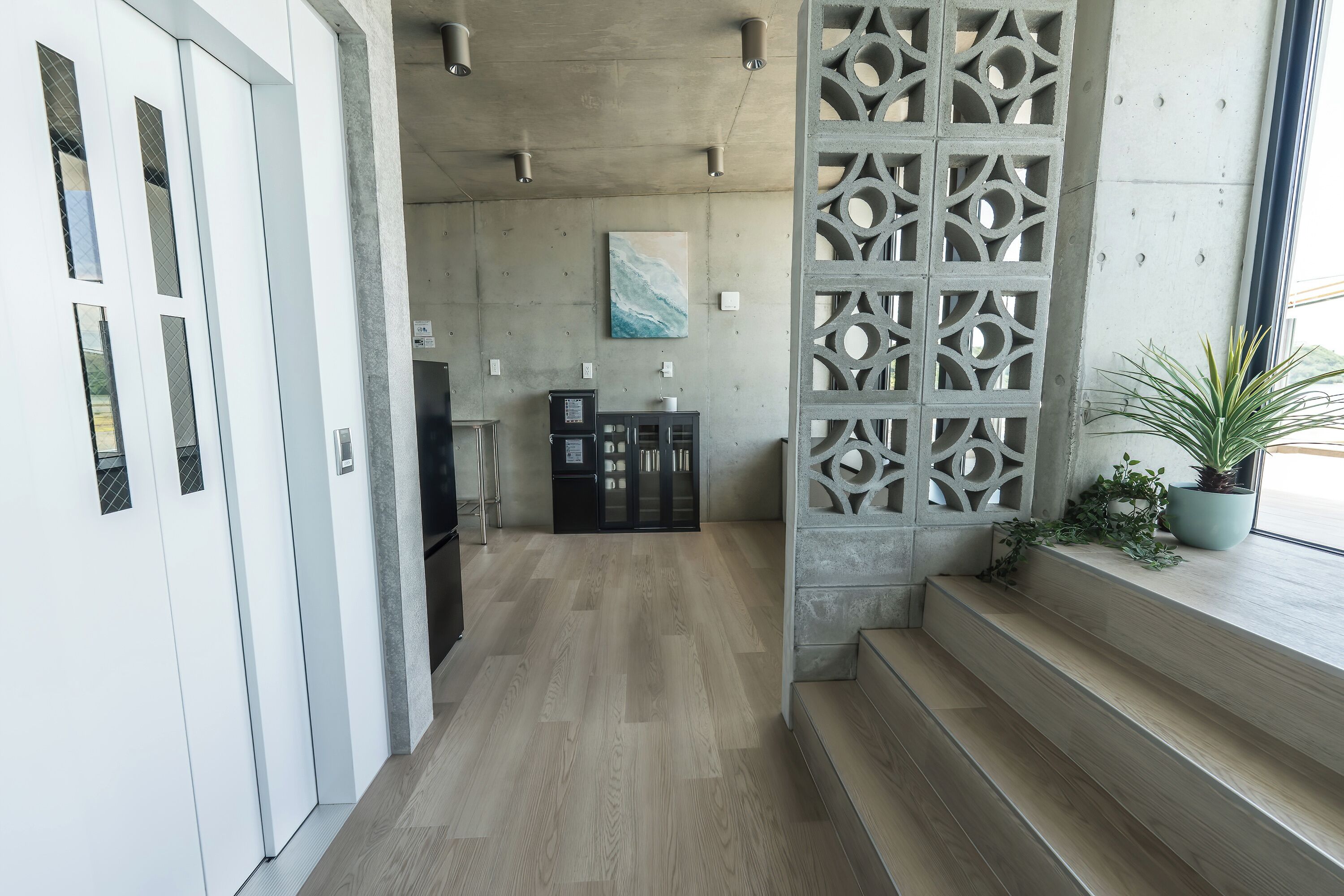A modern interior with a concrete floor, a staircase, a decorative partition, and a refrigerator.