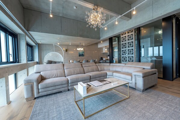 A spacious living area with a large L-shaped sectional sofa, a glass coffee table, and a modern chandelier.