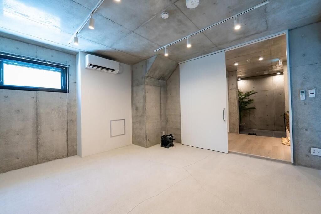 Um quarto espaçoso com teto de concreto, uma janela grande e um aparelho de ar condicionado.