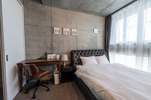 A hotel room with a bed, a desk, a chair, and a window with curtains.