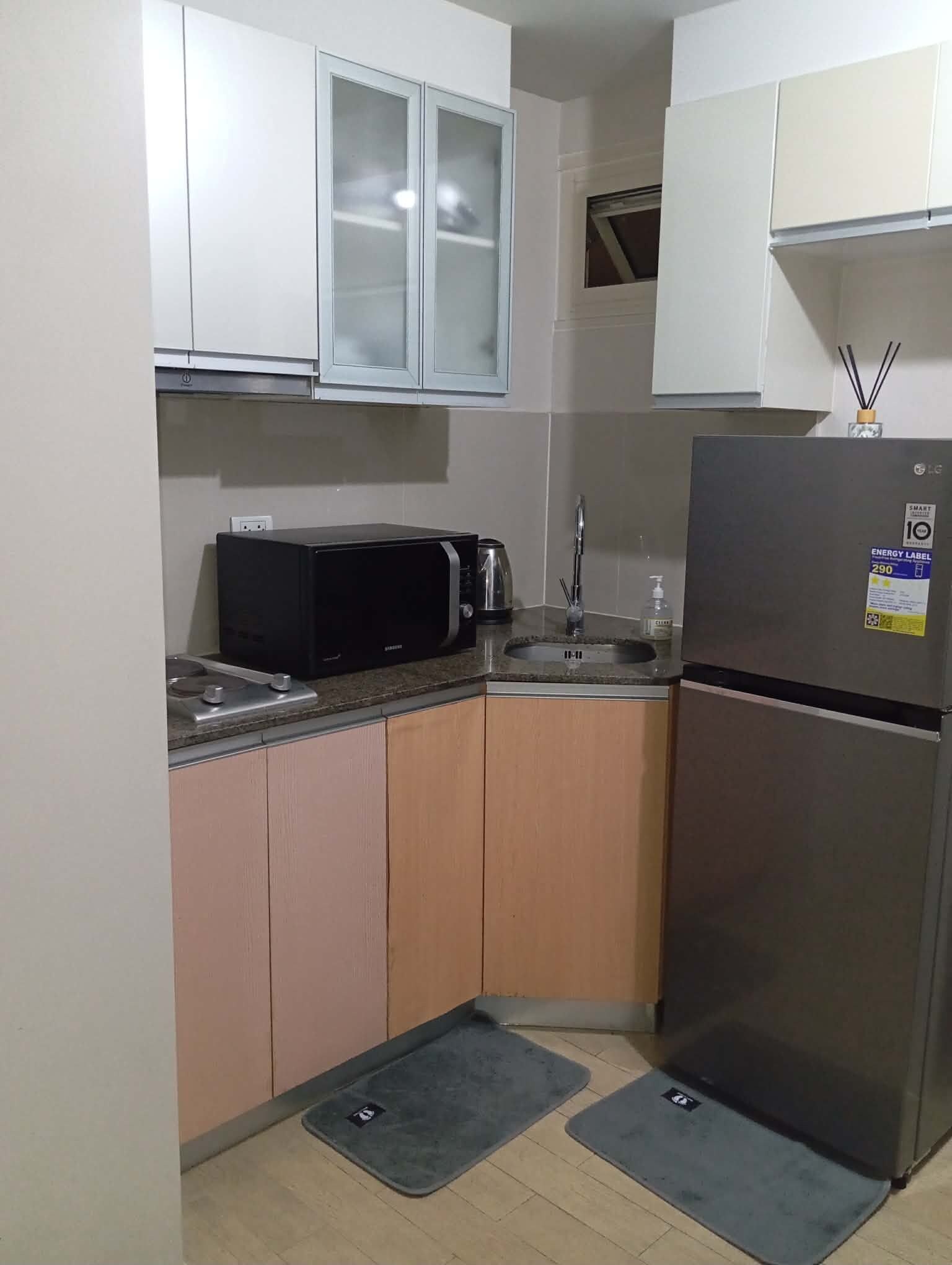 A compact kitchen with white cabinets, a black microwave, a stainless steel refrigerator, and a sink.