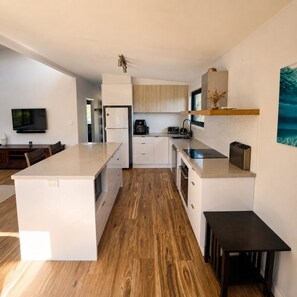 A modern kitchen with a central island, wooden flooring, and a flat-screen TV mounted on the wall.