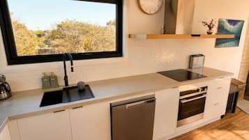 A modern kitchen with a window, built-in dishwasher, oven, and a clock on the wall.