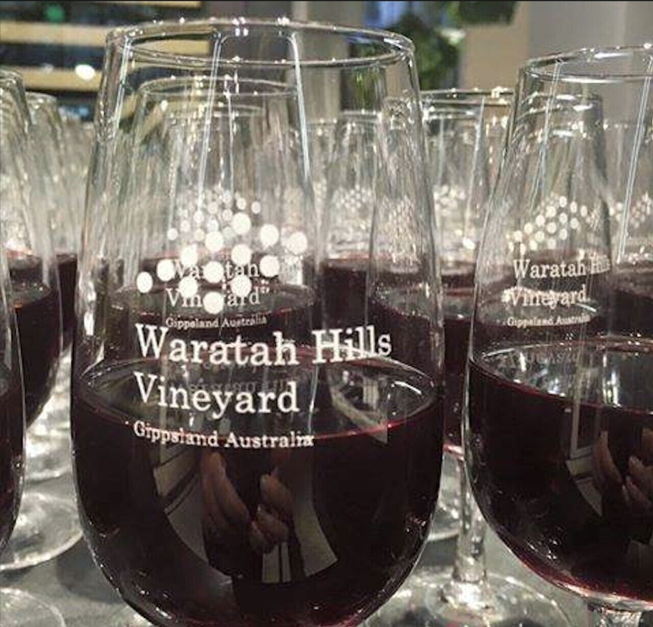 Plusieurs verres à vin remplis de vin rouge, chacun portant l’étiquette « Waratah Hills Vineyard » et « Gippsland, Australie ».