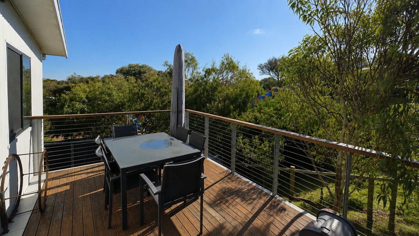 A deck with a table and chairs, surrounded by a metal railing, overlooking a green landscape.