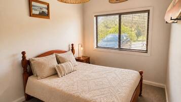 A bedroom with a wooden bed, a hanging light fixture, a window with blinds, and a sign on the wall.