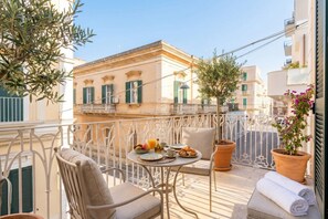 Ein Balkon mit einem Frühstückstisch, ausgestattet mit Früchten, Brot und einem Getränk.