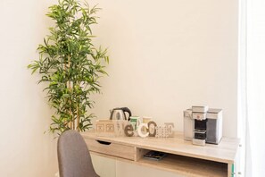 Ein Arbeitsplatz mit Schreibtisch, Kaffeemaschine, Pflanze und einem Schild mit der Aufschrift 'Welcome'.