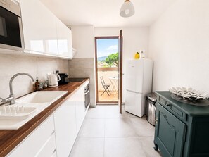 A compact kitchen with a sink, stove, and refrigerator, leading to a patio with a table and chairs. - Air-conditioned apartment, 2 beautiful bedrooms, Beach 10 min walk, Parking (Saint-Cyr-sur-Mer)