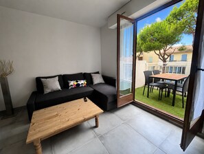 A modern living room with a sofa, a wooden coffee table, and a sliding glass door leading to an outdoor patio with a table and chairs. - Air-conditioned apartment, 2 beautiful bedrooms, Beach 10 min walk, Parking (Saint-Cyr-sur-Mer)