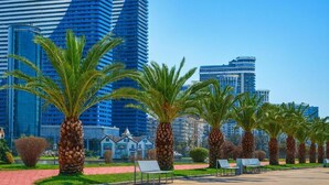 A modern urban park with palm trees and benches, set against a backdrop of high-rise buildings. - Orbi City 2-bedroom apartment in Batumi with air conditioning (Batumi)