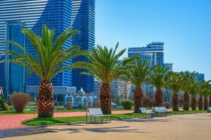 A modern urban park with palm trees and benches, set against a backdrop of high-rise buildings. - Orbi City 2-bedroom apartment in Batumi with air conditioning (Batumi)