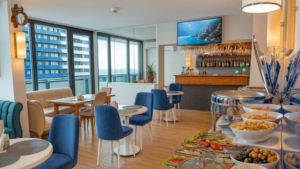 A hotel dining area with round tables, blue chairs, a bar with a TV, and buffet with various dishes. - Orbi City 2-bedroom apartment in Batumi with air conditioning (Batumi)