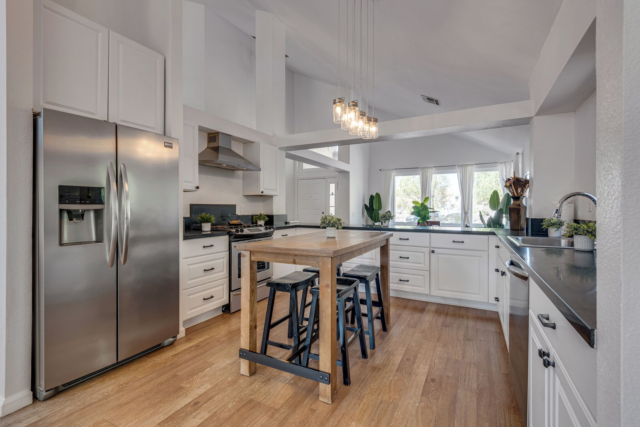 Une cuisine moderne avec des meubles blancs, un réfrigérateur en acier inoxydable, un îlot central en bois avec des tabourets et un luminaire suspendu.