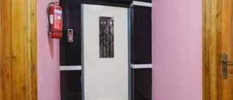A hallway with a white door, a fire extinguisher on the wall, and a wooden door on the right.