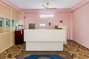 A room with a reception desk, a ceiling fan, a water dispenser, a telephone, a plant, and a patterned rug.
