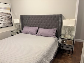 A neatly made bed with a tufted headboard, two bedside lamps, and a framed picture on the wall.