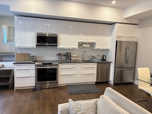A modern kitchen with white cabinets, stainless steel appliances, and a grey rug. - Furnished 2-Bedroom in Wellington Village | 30+ Day Stays** (Ottawa)