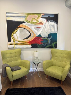 A room with two green armchairs, a black rug, and a large abstract painting on the wall.