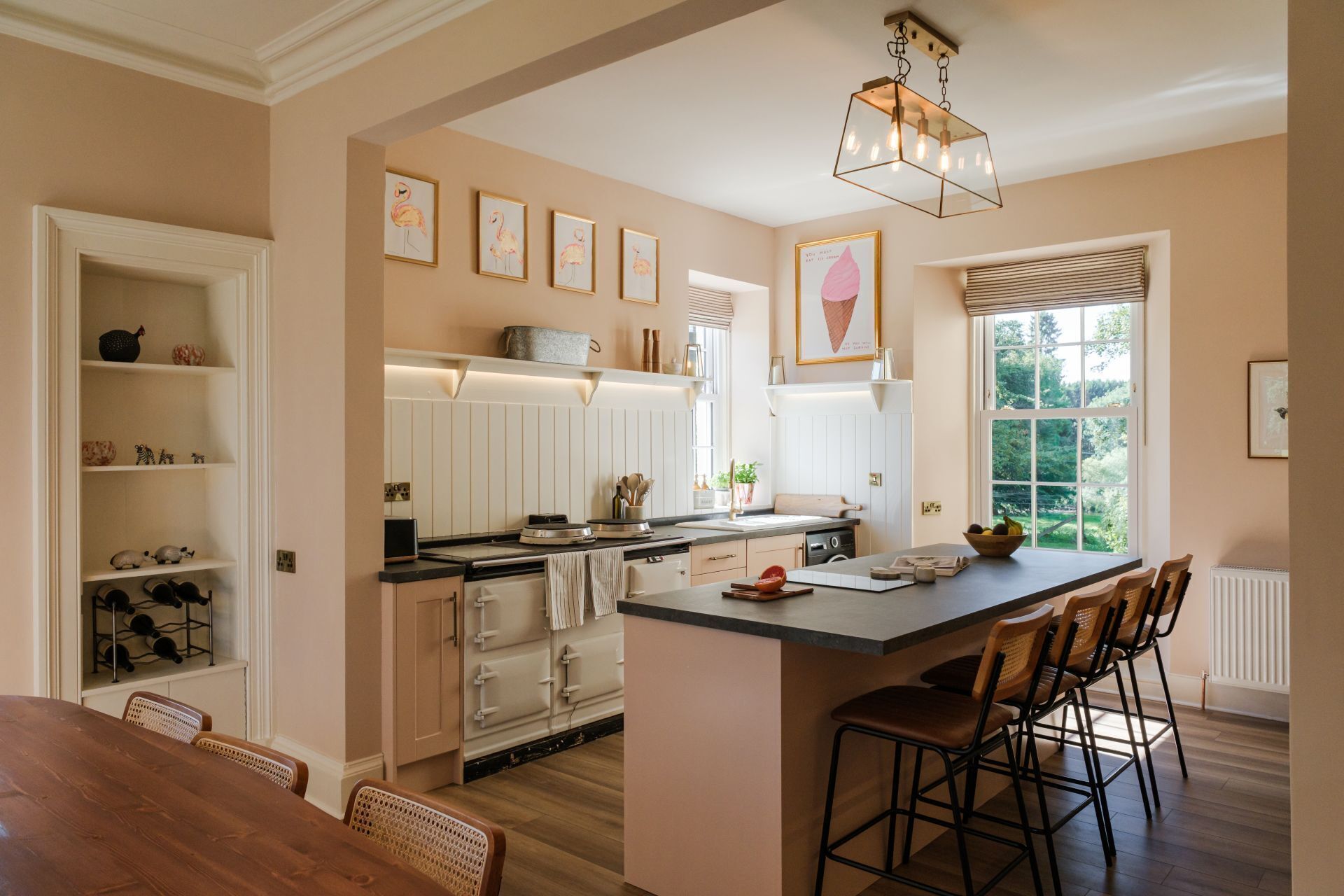 A kitchen with a central island, wooden chairs, a dining table, and a window with a view.