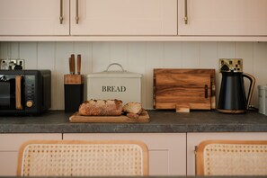 A kitchen with a bread box labeled 'BREAD,' a toaster, a coffee maker, and wooden cutting boards. - Isla Farmhouse - Luxury Cottages (Perth)