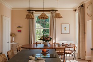 A dining area with a round table, chairs, hanging lamps, a window with curtains, and a clock on the wall. - Isla Farmhouse - Luxury Cottages (Perth)