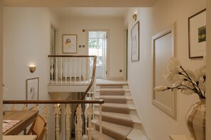 Eine Treppe mit Holzhandlauf führt zu einer Zwischenebene, einem Essbereich mit Tisch und Stühlen, und gerahmte Kunstwerke schmücken die Wände.