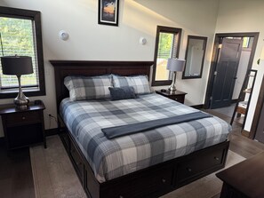 A bedroom with a bed, nightstands, a lamp, a framed picture, and a door.