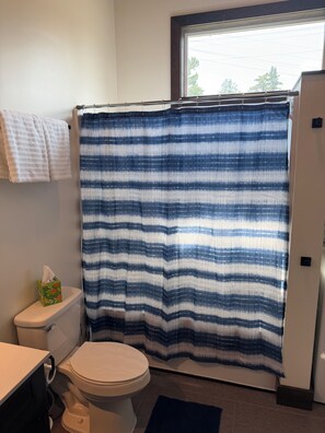 A bathroom with a white toilet, a blue and white striped shower curtain, a white towel hanging on the wall, and a green tissue box on the toilet.