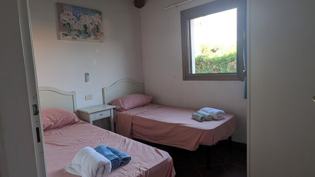 Ein Schlafzimmer mit zwei Einzelbetten, einem Nachttisch, einem kleinen Schreibtisch und einem Fenster.