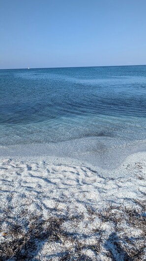 A beach with clear shallow water and a distant sailboat. - Villa Liliana: Your Private Oasis with a Pool (Stintino)