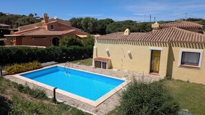 Ein Garten umgibt einen Swimmingpool, in der Nähe befindet sich ein kleines Gebäude.