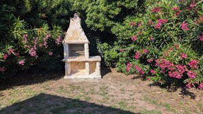 Ein Steingrill mit Schornstein, umgeben von grünem Laub und pinkfarbenen Blütenpflanzen.