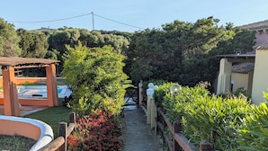 Ein Kiesweg führt durch einen Garten, mit einem Holzzaun auf der einen Seite und einem Poolbereich auf der anderen.