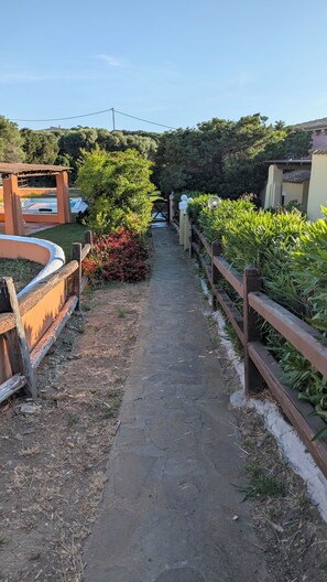 A stone pathway leading through a garden with a wooden fence on one side and a pool area on the other. - Villa Liliana: Your Private Oasis with a Pool (Stintino)