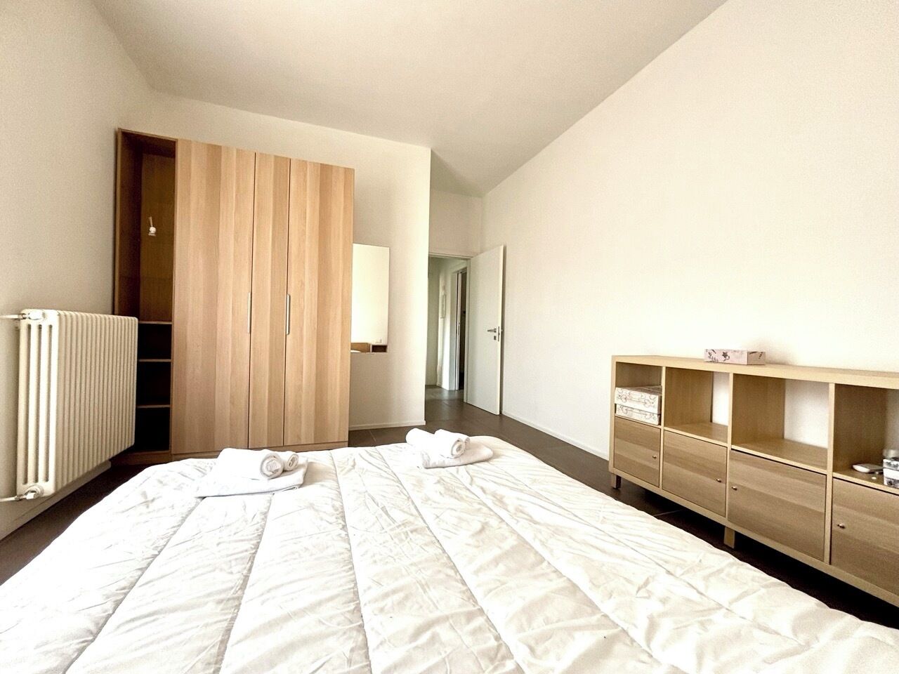 Een hotelkamer met een groot bed, een houten garderobe, een radiator en een klein kastje.