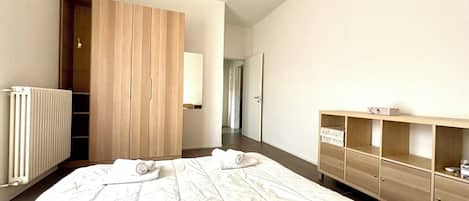 Een hotelkamer met een groot bed, een houten garderobe, een radiator en een klein kastje.