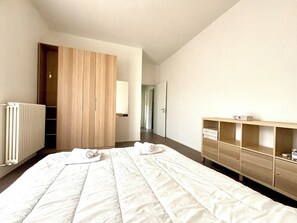 Une chambre d’hôtel avec un grand lit, une armoire en bois, un radiateur et un petit meuble.