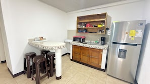 A compact kitchen with a refrigerator, a microwave, a sink, and a wooden cabinet above the counter.