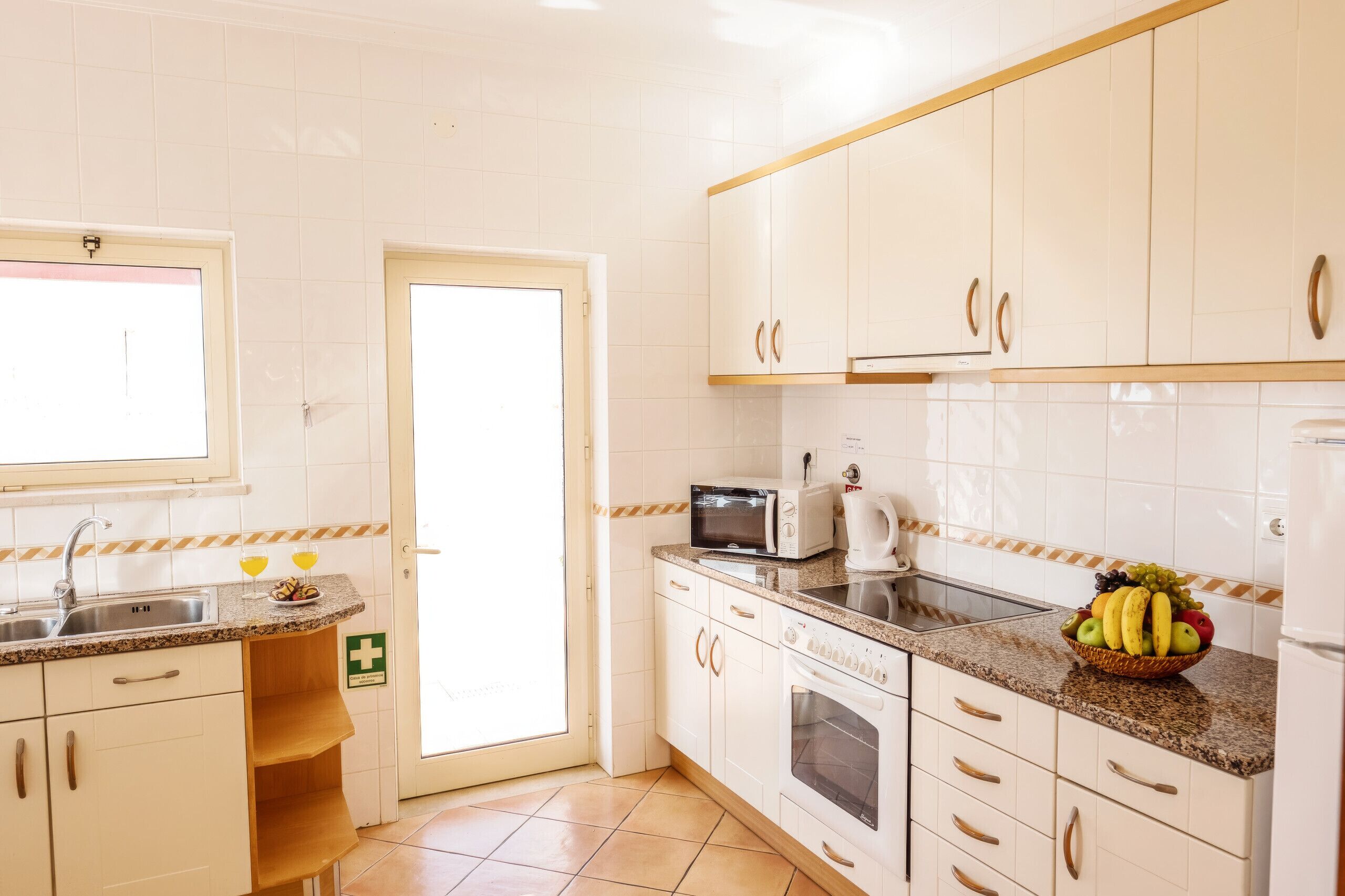 A kitchen with white cabinets, a microwave, a kettle, and a fruit bowl on the counter.