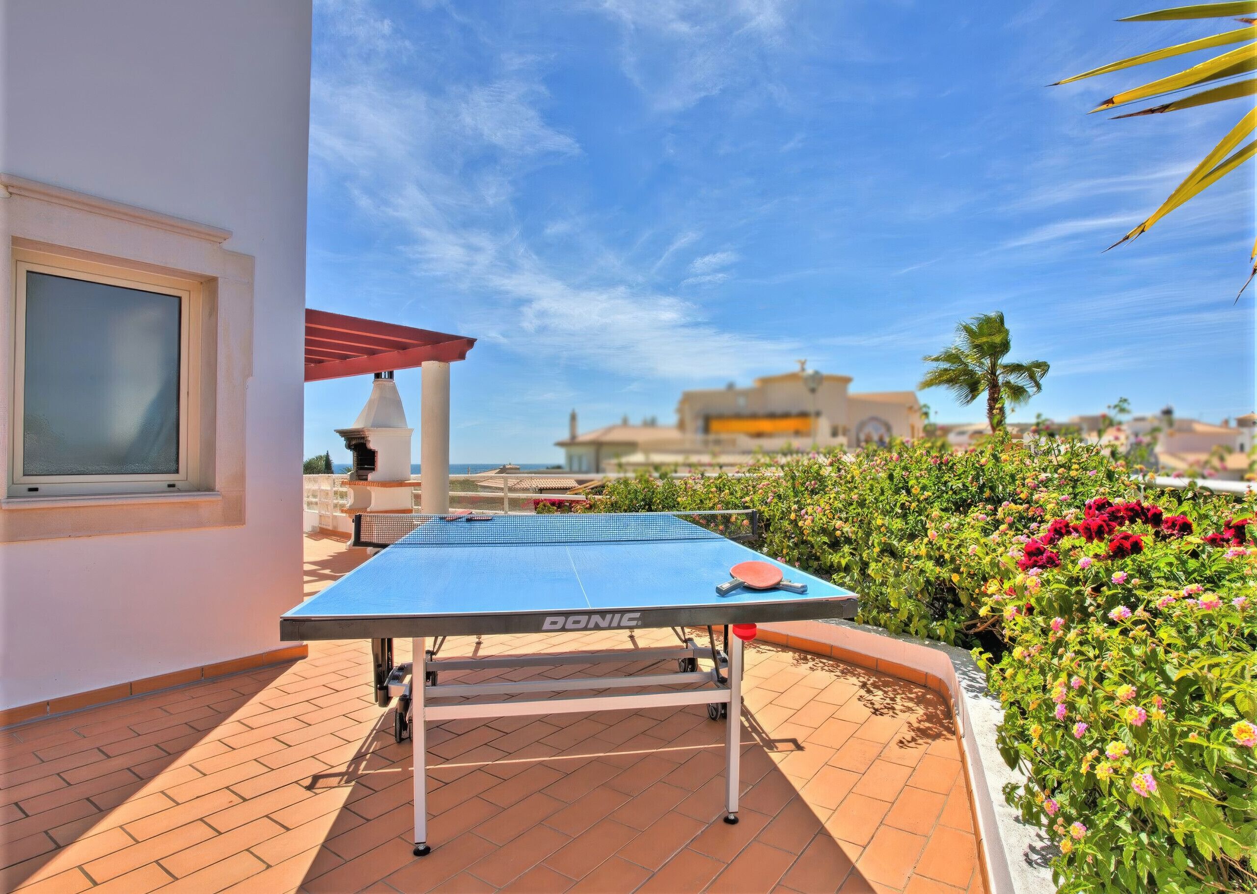 Un tavolo da ping pong su una terrazza con vista libera sul mare e edifici sullo sfondo.