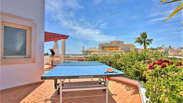 Un tavolo da ping pong su una terrazza con vista libera sul mare e edifici sullo sfondo.
